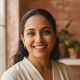 Close-up portrait of a smiling South Asian woman, 30s, with a friendly and trustworthy expression, against a blurred terracot