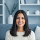 A happy young Latina woman with smooth, shiny dark hair smiles confidently, with a soft slate blue and white background.